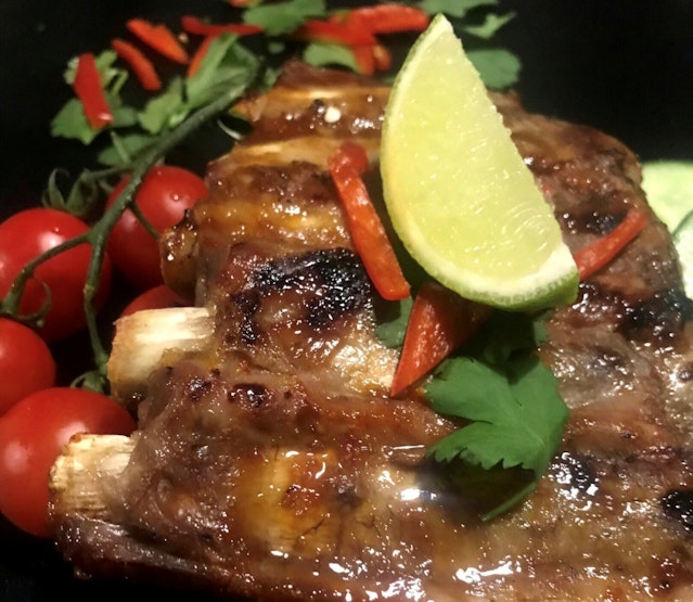 A plate of alcohol-free whisky infused pork ribs with chilli and lime glaze. Served with salad and a wedge of lime.