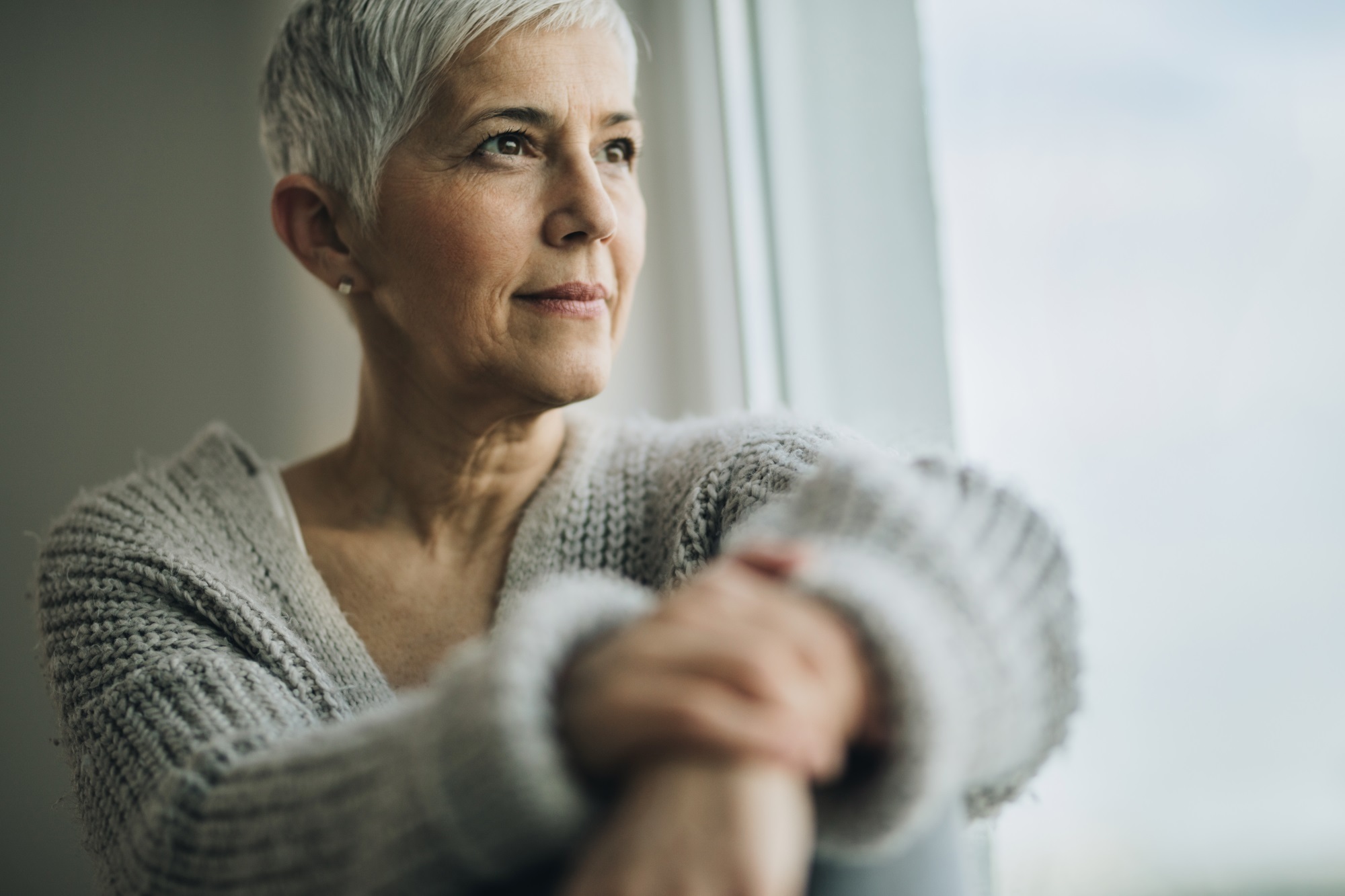 An older woman with short, cropped hair looks out of a window.