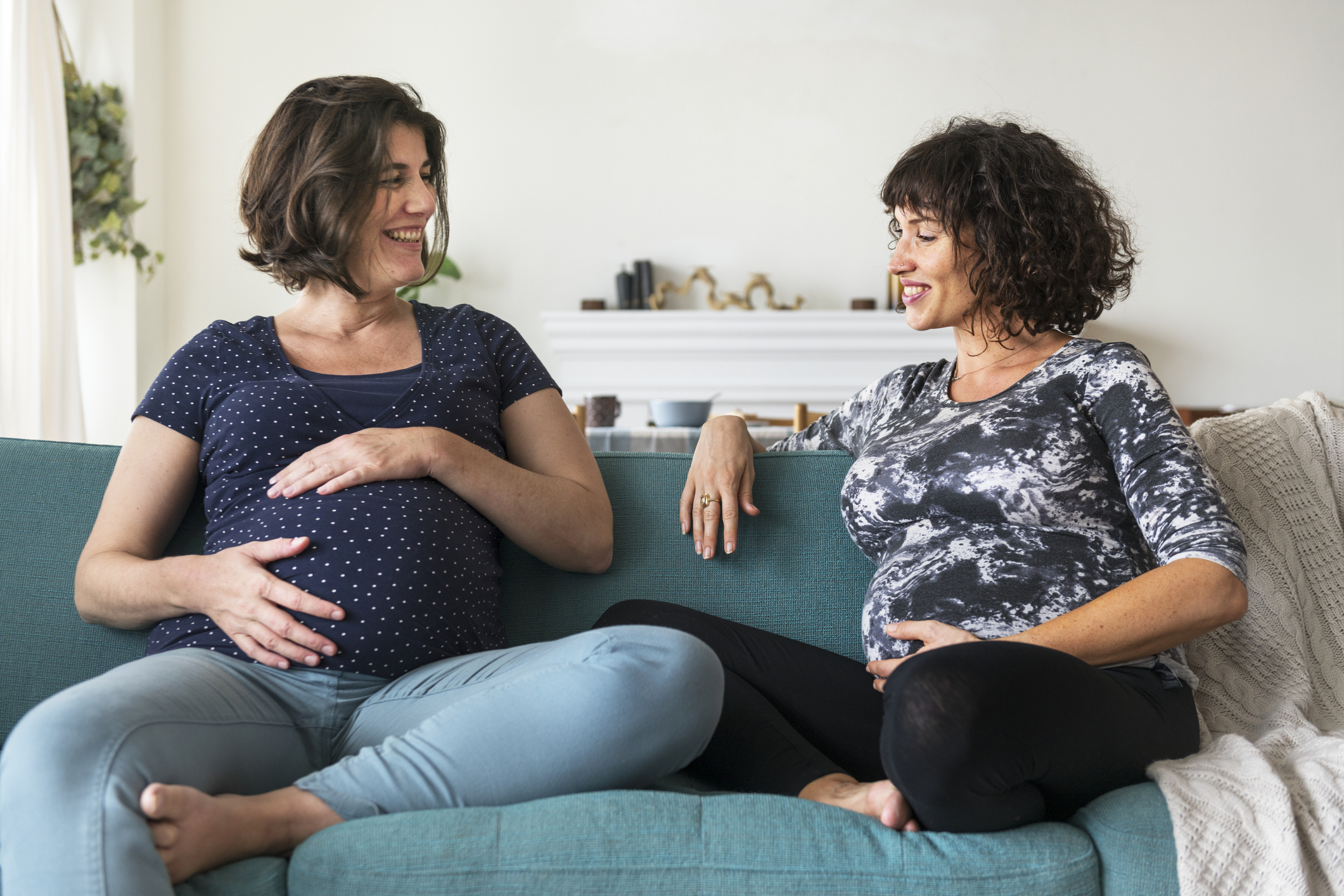 Pregnant friends relaxing on sofa at home talking together
