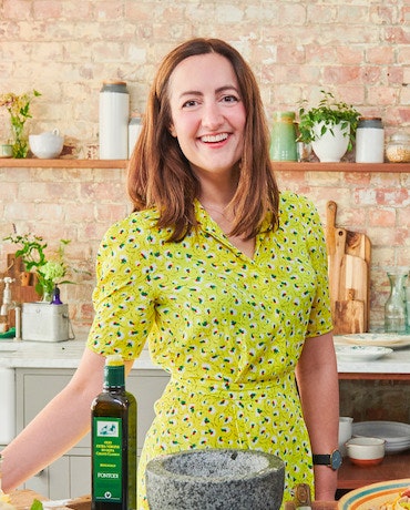 A woman wearing a green shirt in a kitchen smiles.