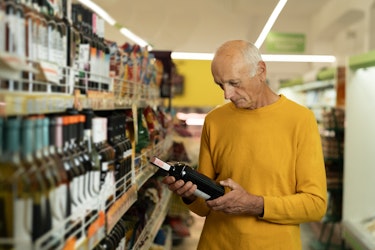 Elderly man chooses wine in the supermarket. Senior man reads the label on a bottle of wine before buying.