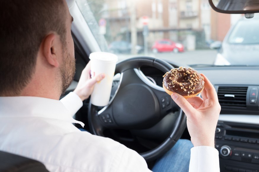 A man eats a donut whilst driving his car.