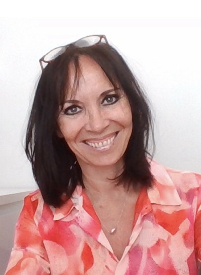 A woman with dark hear wearing a pink shirt smiles.
