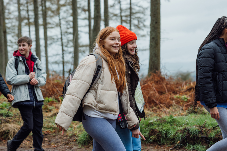 Side view of a group of teenagers on an educational walk through the woods.
