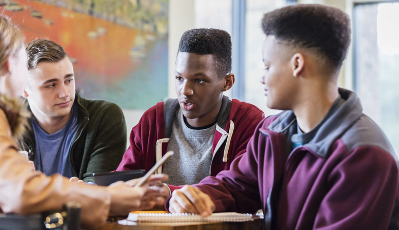 A group of four teenage friends, sitting at a table having a discussion.