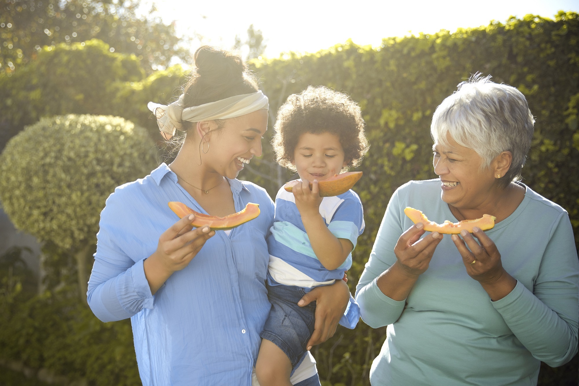 Three generations enjoying papaya on a sunny day in their garden at home