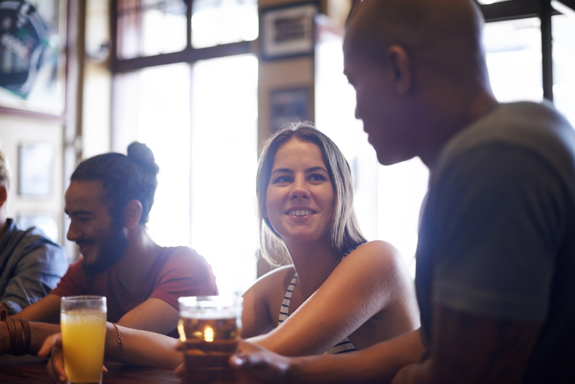 Three people a woman and two men chat in a bar The woman drinks orange juice and smiles at one of the men i Stock 497155057 2000 px
