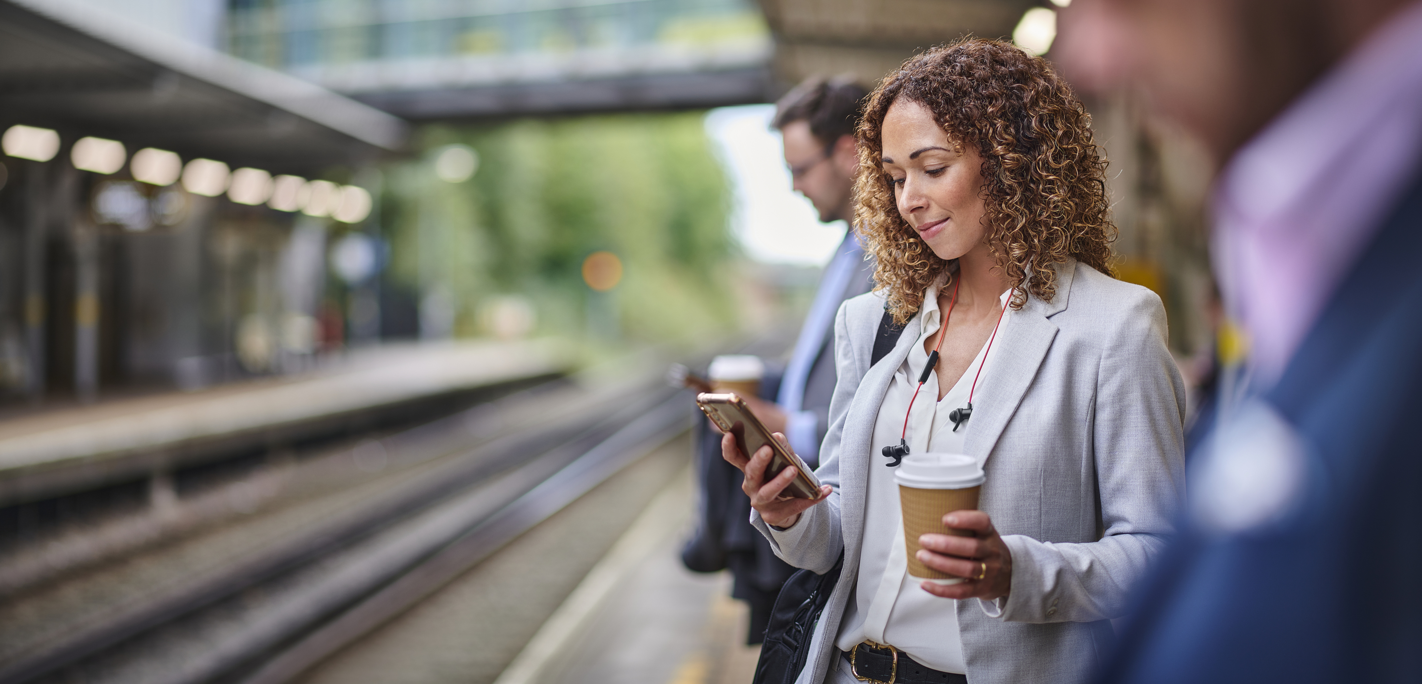 Young woman commuter on train platform looking at her phone while holding a coffee