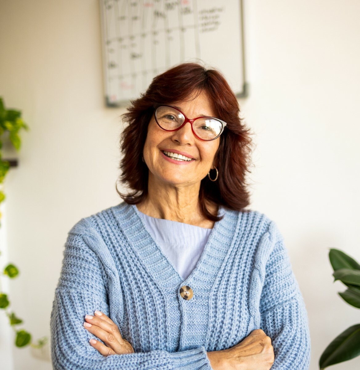 A mature woman with dark hair wearing glasses and a blue cardigan smiles broadly at the camera.