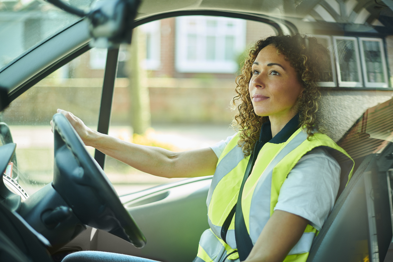 Female delivery driver driving van wearing high visibility jacket