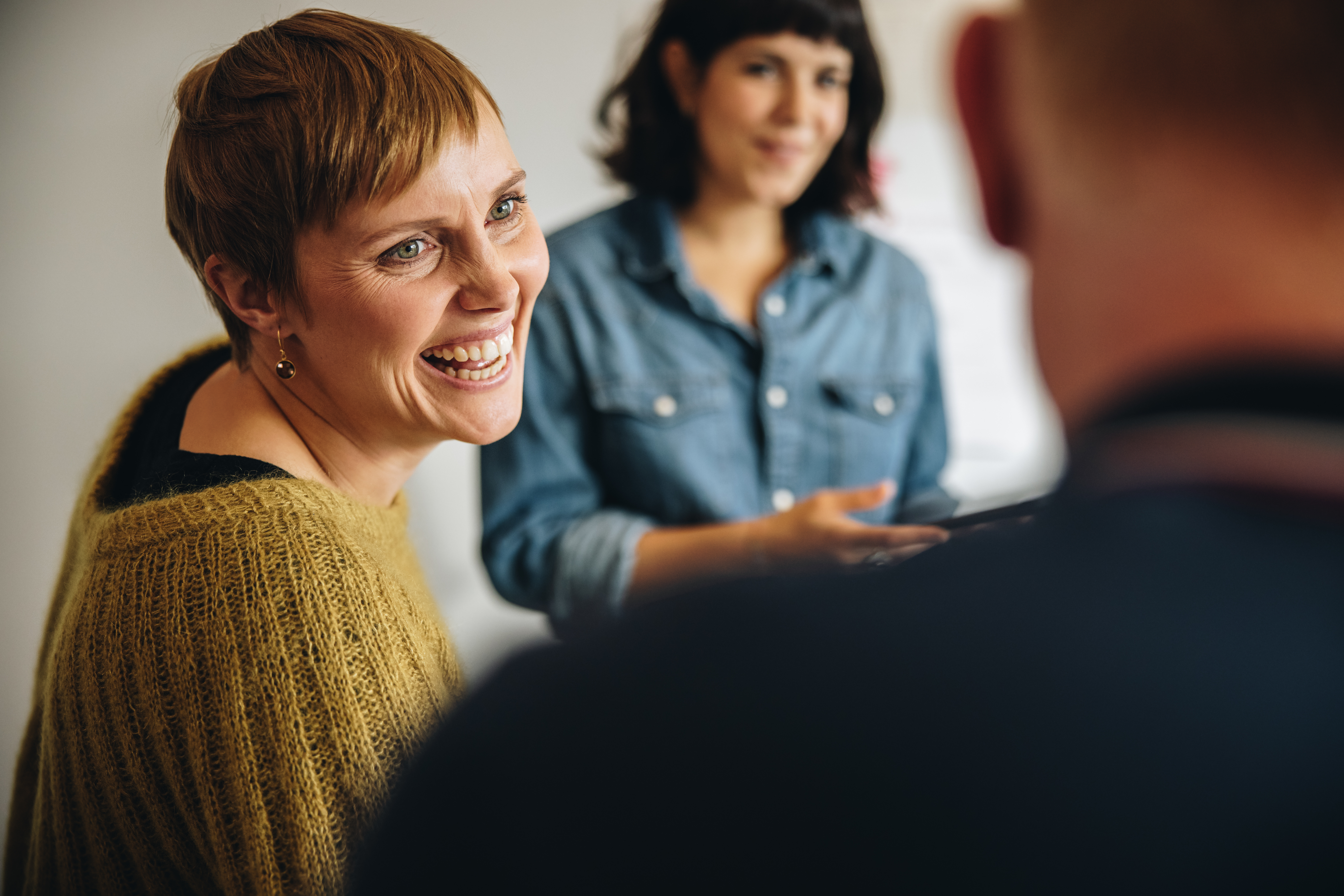 A woman sitting in a group indoors smiles.