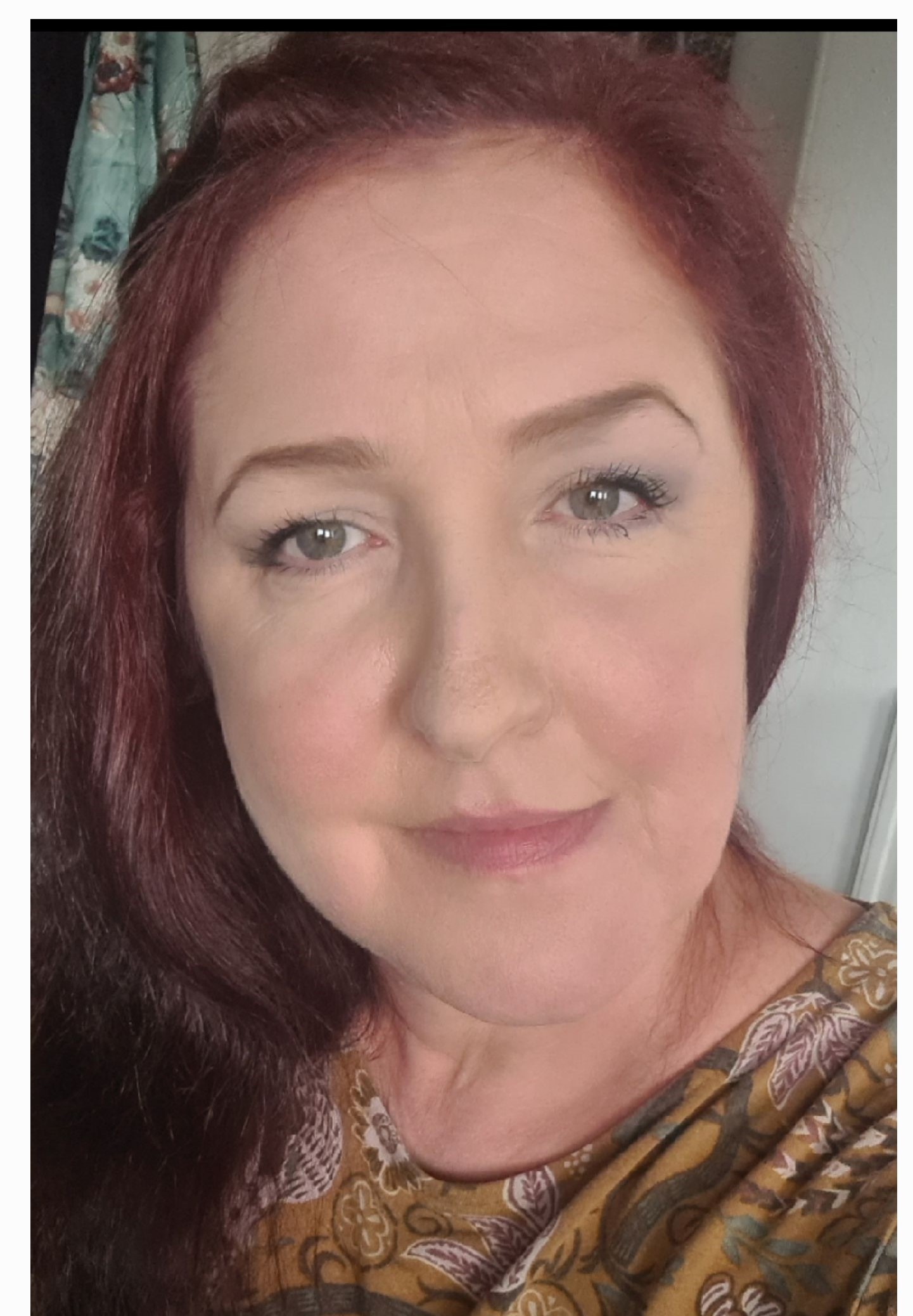 A woman with died red hair smiles at the camera.