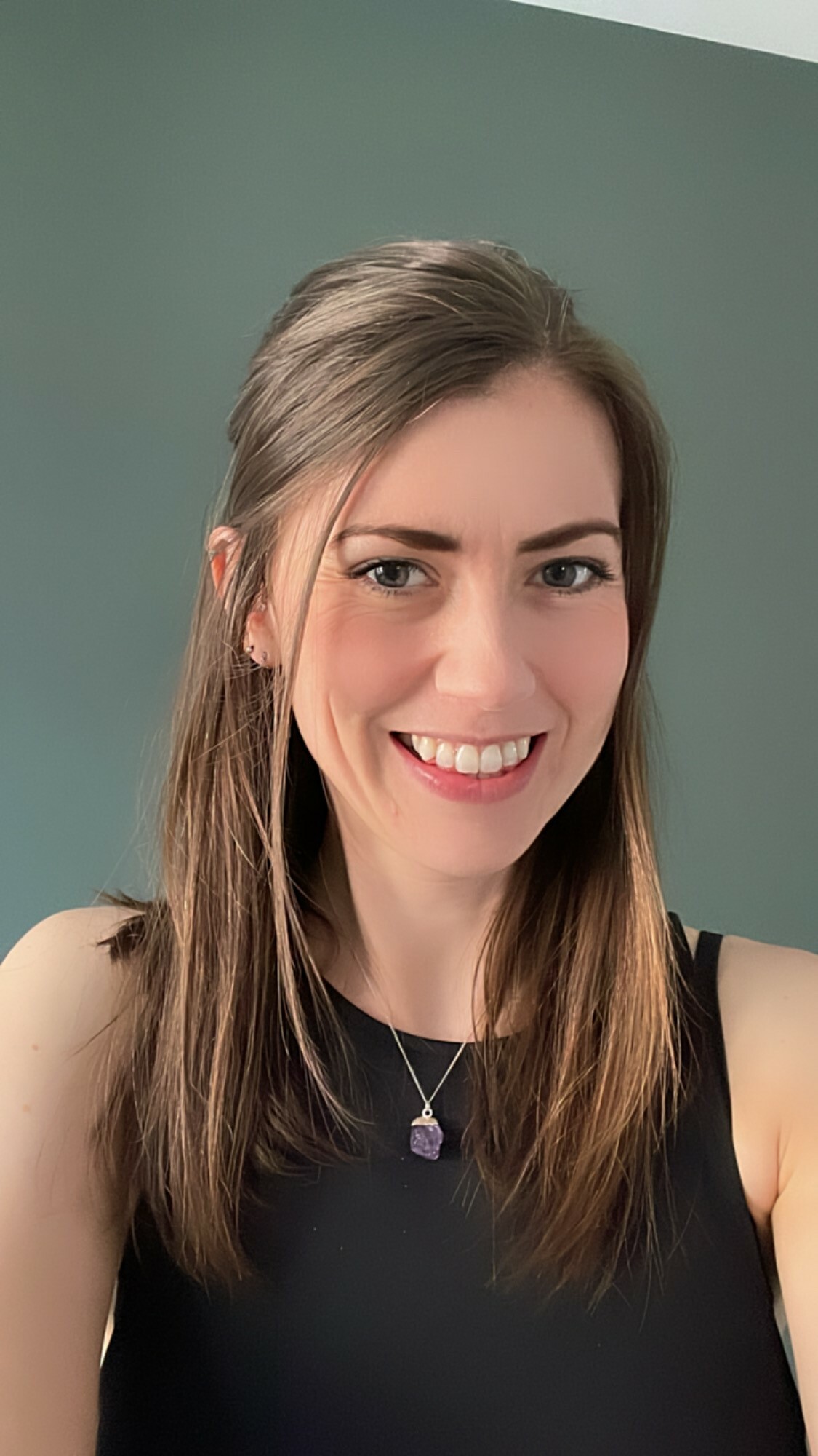 A woman in a black vest top smiles at the camera.